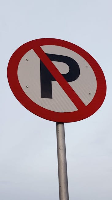A row of traditional terraced houses in Teddington with brick facades, white bay windows, and pitched tiled roofs, lining a residential street. Several cars are parked along the curb, including a white vehicle directly in front of a house with a small front garden and black iron fence. Street lighting posts and overhead power lines are visible above the pavement. The street appears quiet with no visible people or movement, suggestive of a typical home relocation or local move setting. This scene complements house removals and furniture transport services offered by Man and Van Teddington, especially considering the narrow street that may require careful planning during the loading and unloading process for packing and moving projects.